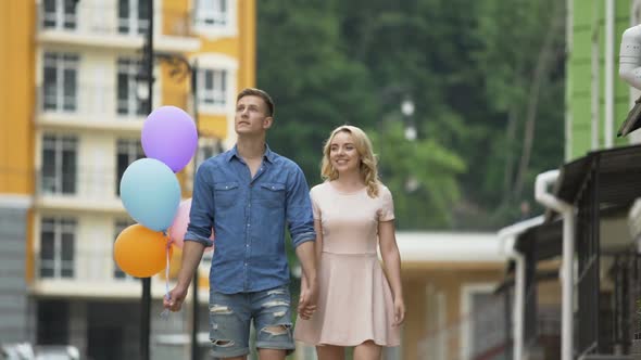Girlfriend and Boyfriend with Balloons Walking Down Street, Stopping to Kiss