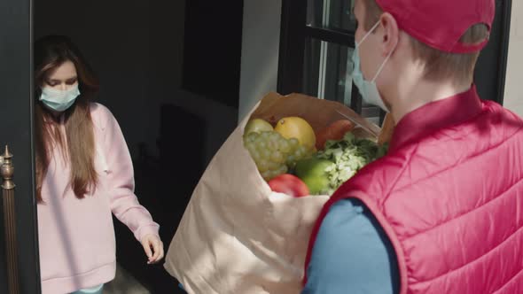 Postman or Delivery Man in Mask During Coronavirus Carry Small Box Food Deliver to Young Woman