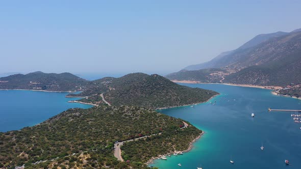 Aerial drone panning left across a peninsula full of large green hills in Kas Turkey and anchored bo