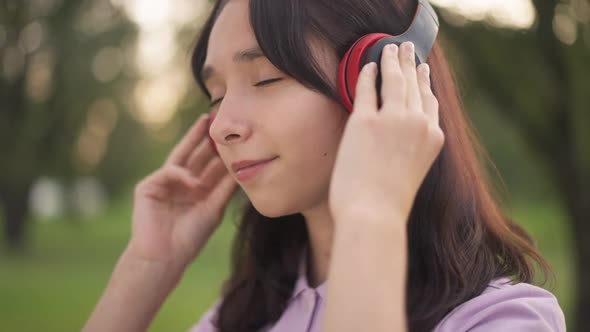Headshot Portrait of Teenage Caucasian Girl in Headphones Enjoying Music with Closed Eyes Outdoors