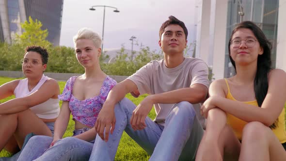 Group of multiethnic young friends sitting outdoor together overlooking smiling