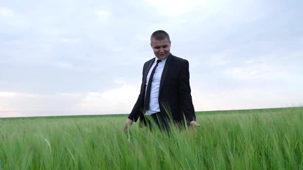 Happy Young Farmer in a Suit Walks on a Green Wheat Field