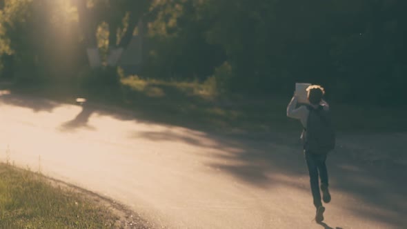 Happy Pupil in Jeans Runs Along Road and Throws Sheets