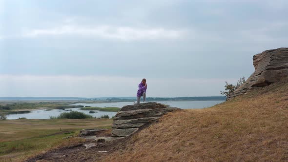 A Girl is Doing Fitness on a Hill on the Lake Shore