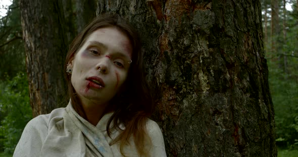 Close-up Portrait of a Brutally Beaten Woman in the Woods Pressed Against a Tree