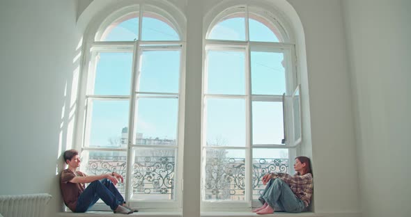 a Man and a Woman Sit on the Windowsill of the Window Looking Away From Each Other