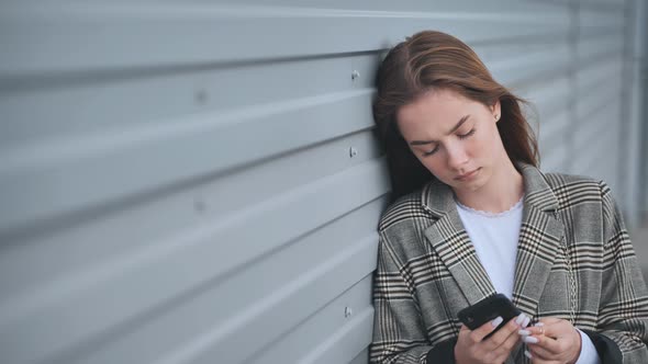 A Disgruntled Girl Stares Into a Smartphone Against a Striped Wall