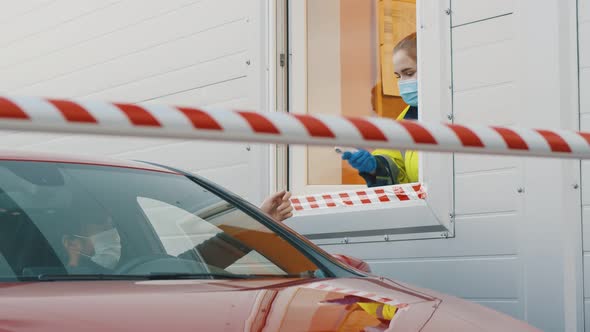 Worker in Booth Wearing Protective Mask and Gloves Checking Temperature of Male Driver