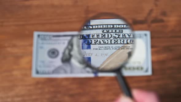 One Hundred Dollars Inspects Under Magnifying Glass on Wooden Table