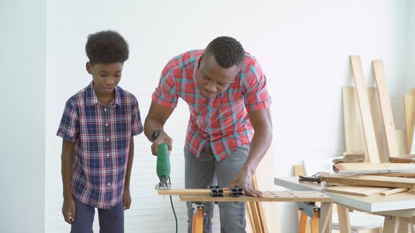 Curious child boy watch and learn his father cutting a piece of wood with a electric saw in factory