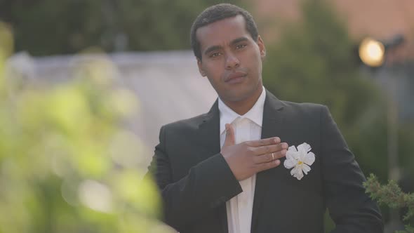 Smiling Groom or Best Man Holding Hand on Chest Looking at Camera Standing in Sunlight Outdoors