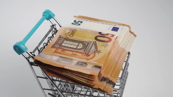 A wad of euro money falls on an empty consumer mini shopping cart