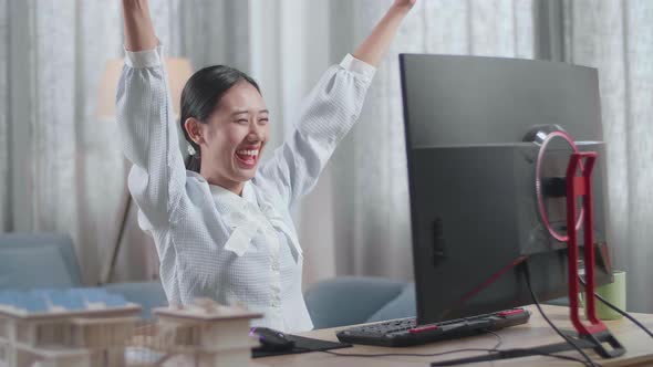 Asian Woman Engineer With The House Model Celebrating While Working On A Desktop At Home