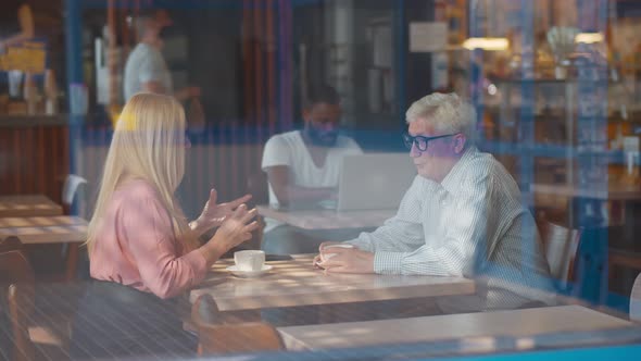 View Through Window Ofn Senior Couple in Love Sitting in Cafe Talking and Drinking Coffee