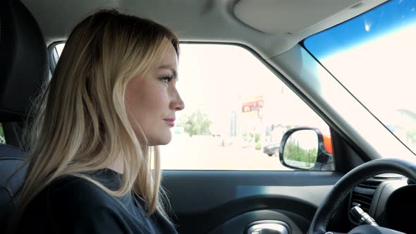 Blonde Young Woman is Driving a Car in the City
