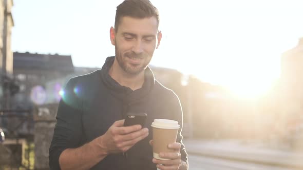 Happily Smiling Attractive Man Walking down the Street chatting uding Smartphone