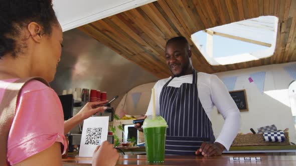 Happy female customer paying smiling african american male food truck owner by smartphone