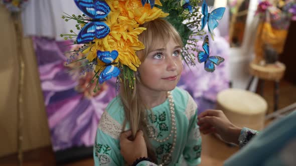 Portrait of Charming Girl in Head Wreath with Flowers and Butterflies Looking Up Standing Indoors As