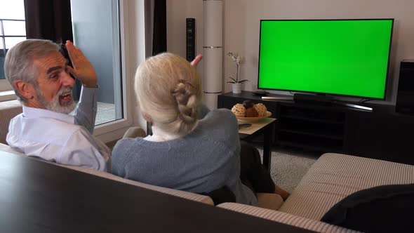 An Elderly Couple Sits on A Couch in A Living Room, Watches Tv with A Green Screen and Celebrates