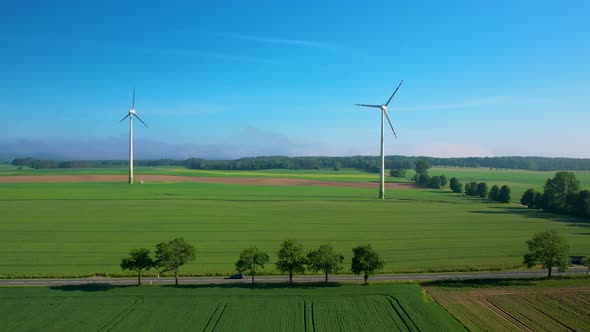 Wind Turbines generating electricity over lush farmlands. Aerial.