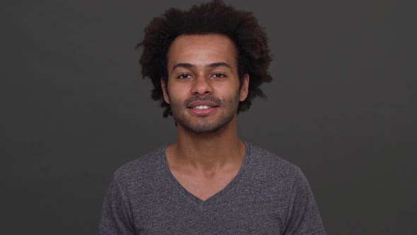 Dark Skinned Young Man with Afro Haircut Smiling with White Teeth and Winking Isolated Over Charcoal