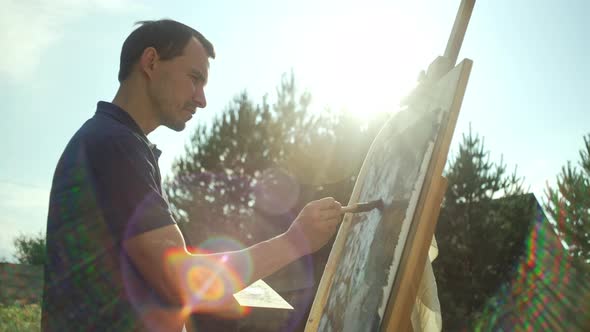 A Male Artist Paints a Picture on an Easel with a Brush