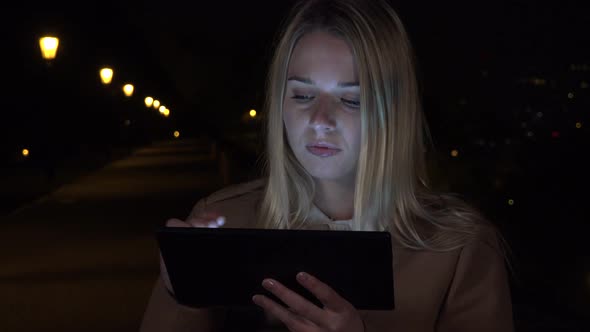 A Young Beautiful Woman Works on a Tablet in an Urban Area at Night