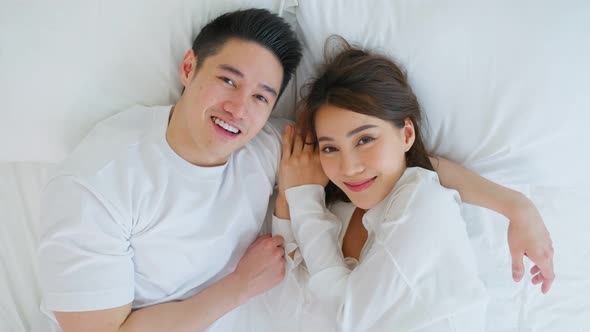 Portrait of Asian new marriage couple lying on bed and look each other.