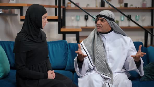 Irritated Annoyed Middle Eastern Man in Traditional Clothing Arguing with Dissatisfied Woman Sitting