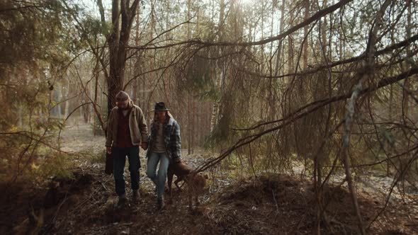Couple Holding Hands and Walking with Dog in Woods