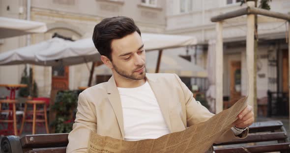 Young Man Sitting On A Bench And Reading An Interesting Article