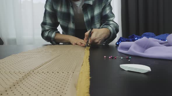 Woman cutting fabric with scissors in tailor's studio, soap slice, safety pins lying on table.