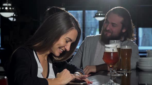 Beautiful Happy Woman Using Her Smart Phone, Drinking Beer with Friends