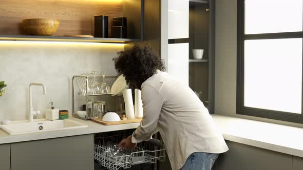 Muslim Man Takes Clean Glasses Out of Dishwasher in Kitchen