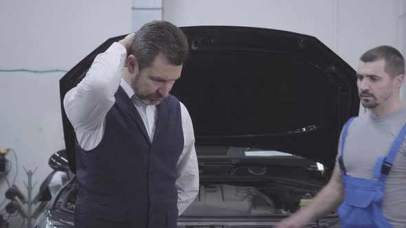 Portrait of Upset Caucasian Businessman Standing in Front of Open Car Hood and Thinking As Auto