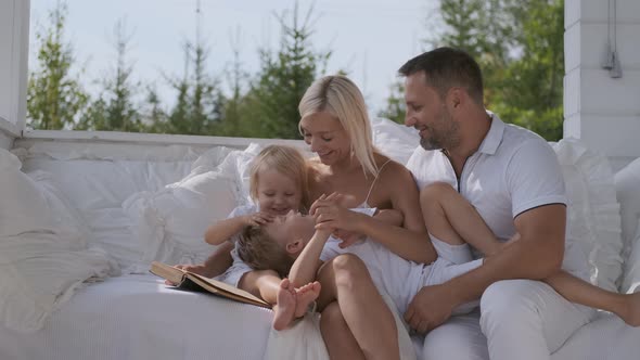 Young Happy Family Mom Dad and Two Sons Having Fun Sitting on a Bright Veranda Near the House