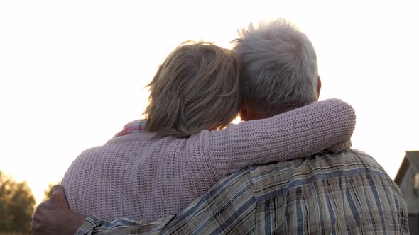 Elderly Old Couple In Love Hugs Against Of Sunlight At Sunset At Summer Fall