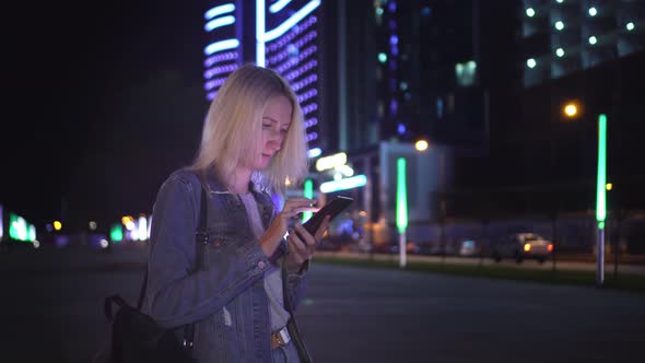 woman uses smartphone to communicate in night city. against backdrop skyscrapers