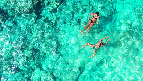 Pretty fun women on photoshoot enjoying life on the beach on clean white sand and blue 4K background