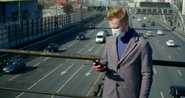 Alone Young Man with Face Mask Is Using Smartphone on Street at Sunny Spring Day