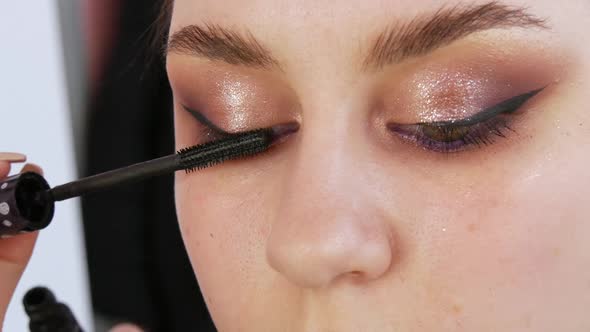 Stylist Makeup Master Applies Mascara to the Eyelashes of a Young Model with a Special Brush Evening