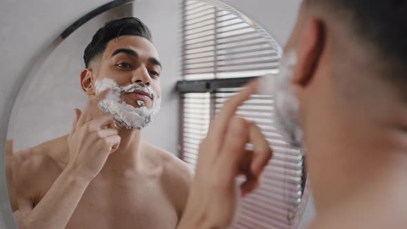 Arab Indian Bearded Man Naked Guy Looks at Reflection in Mirror Applies White Foam Shaving Gel Male