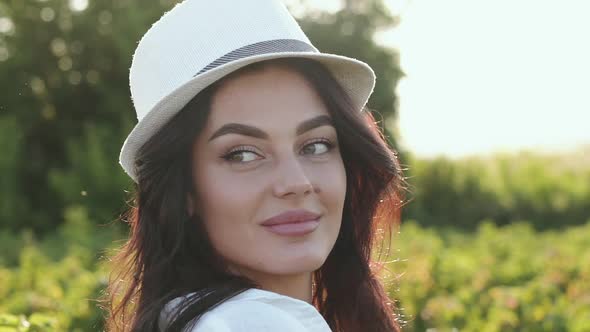 Charming Brunette in Hat Smiling Looking Around and at Camera in Field