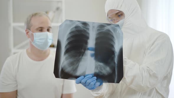 Blurred Doctor in Antiviral Suit Talking To Mid-adult Man in Face Mask Showing Covid-19