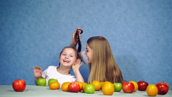 Girls at table with fruit. Woman having fun with girl at table with fruit