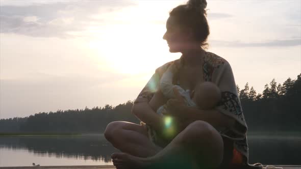 Young Mom Breastfeeding Her Baby on the Dock of the Lake at sunset.Mother Baby Bonding Time.