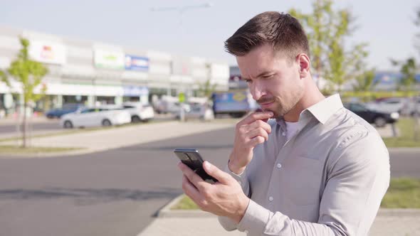 A Young Caucasian Man Works on a Smartphone in an Urban Area