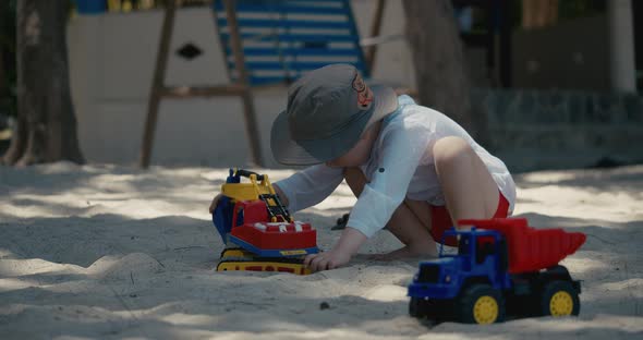 Children Plays with a Plastic Car in the Sand on the Beach