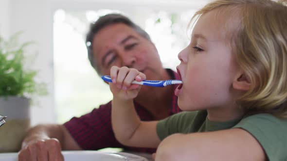 Caucasian grandfather helping his grandson to brush his teeth at home