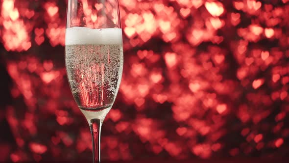 Champagne Is Poured Into a Glass on a Red Background with Many Hearts Close Up